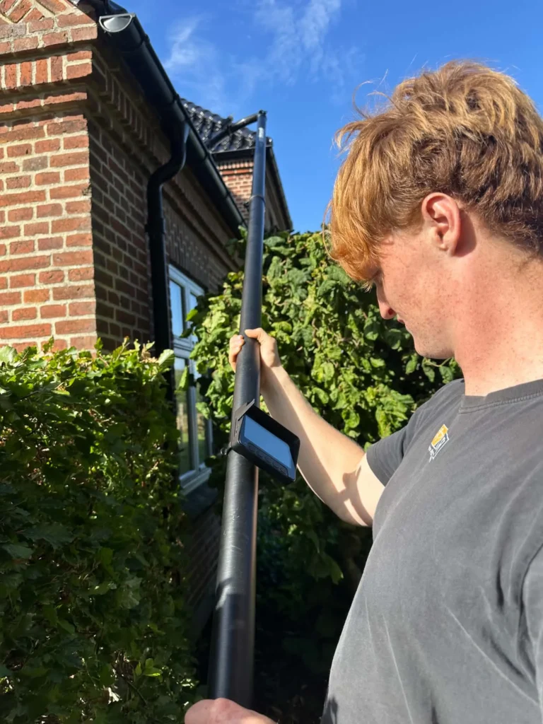 Rensning af tagrende med kamera og skærm på teleskopstangen, så resultatet kan ses fra jorden