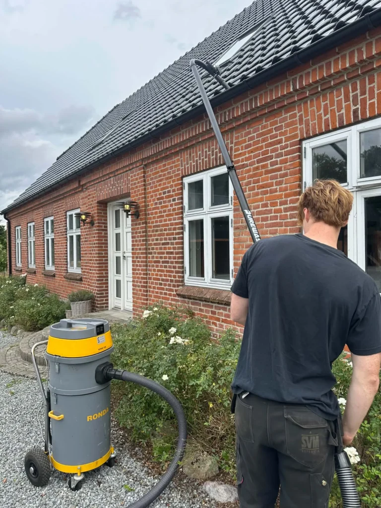 Rensning af tagrende fra jorden med teleskopstang på murstenshus