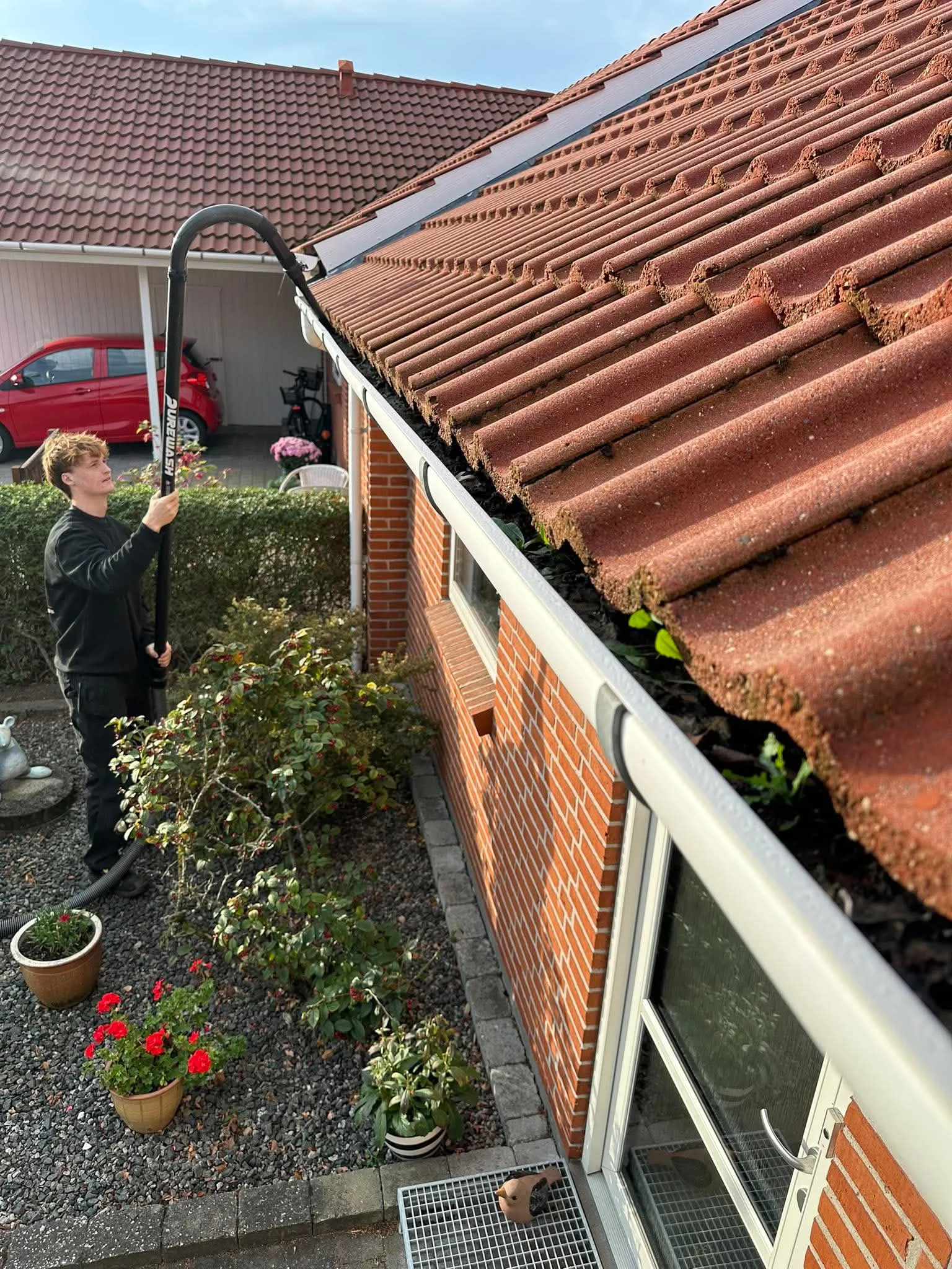 Tagrende fyldt med planter på et rækkehus i Galten bliver renset fra jorden med sugeudstyr på teleskopstang